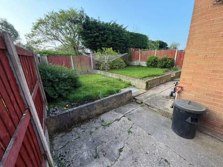 The same garden from the same spot before the work, with cracked concrete and a tired lawn.