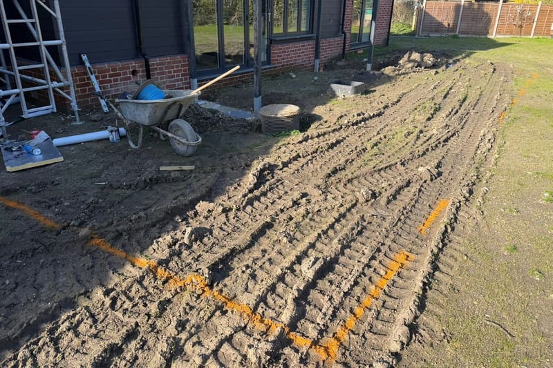 The same ground set out in orange marker spray, with a drainage chamber and a gully sitting in the dug earth.